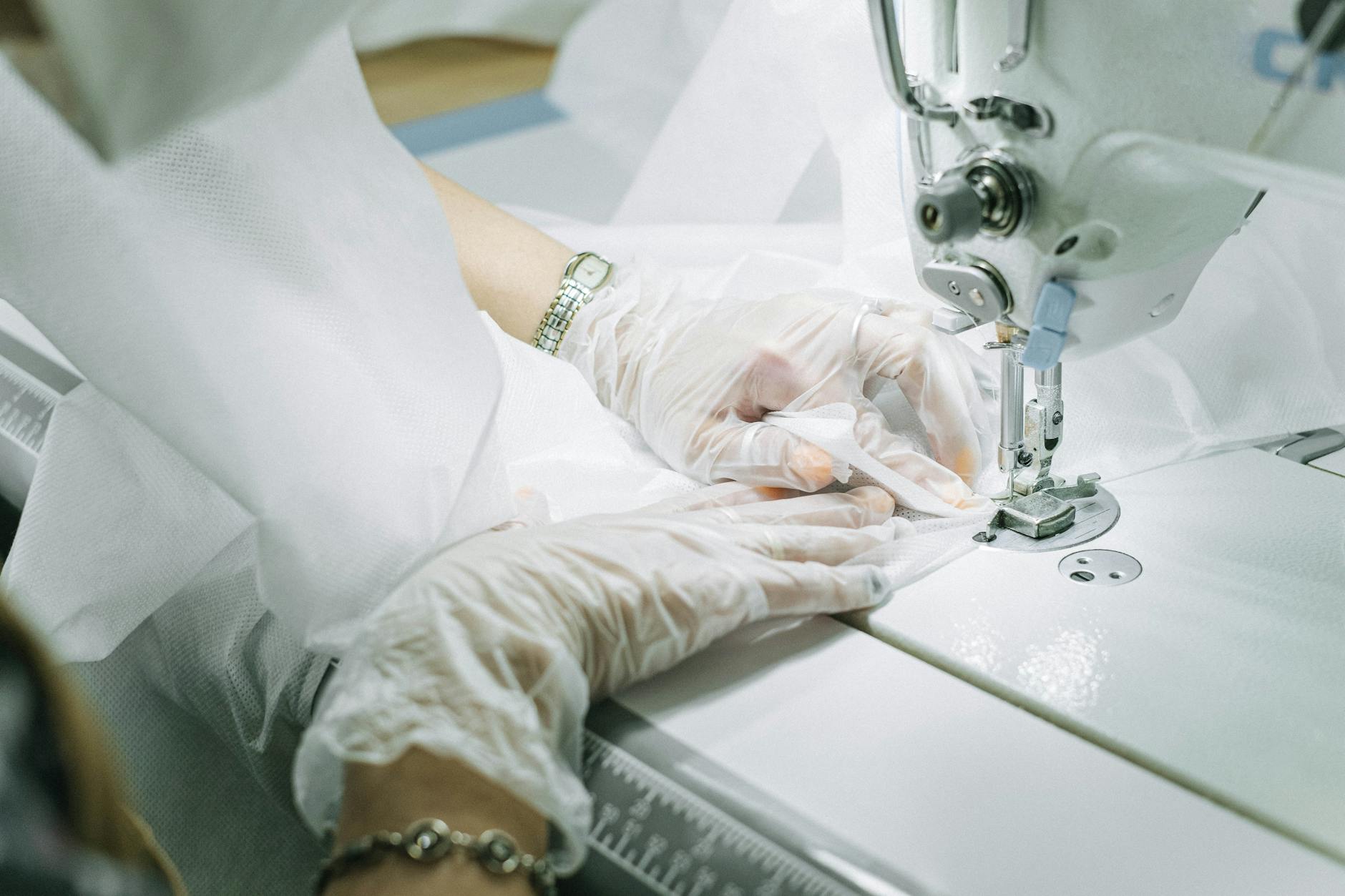 person wearing plastic gloves using a sewing machine